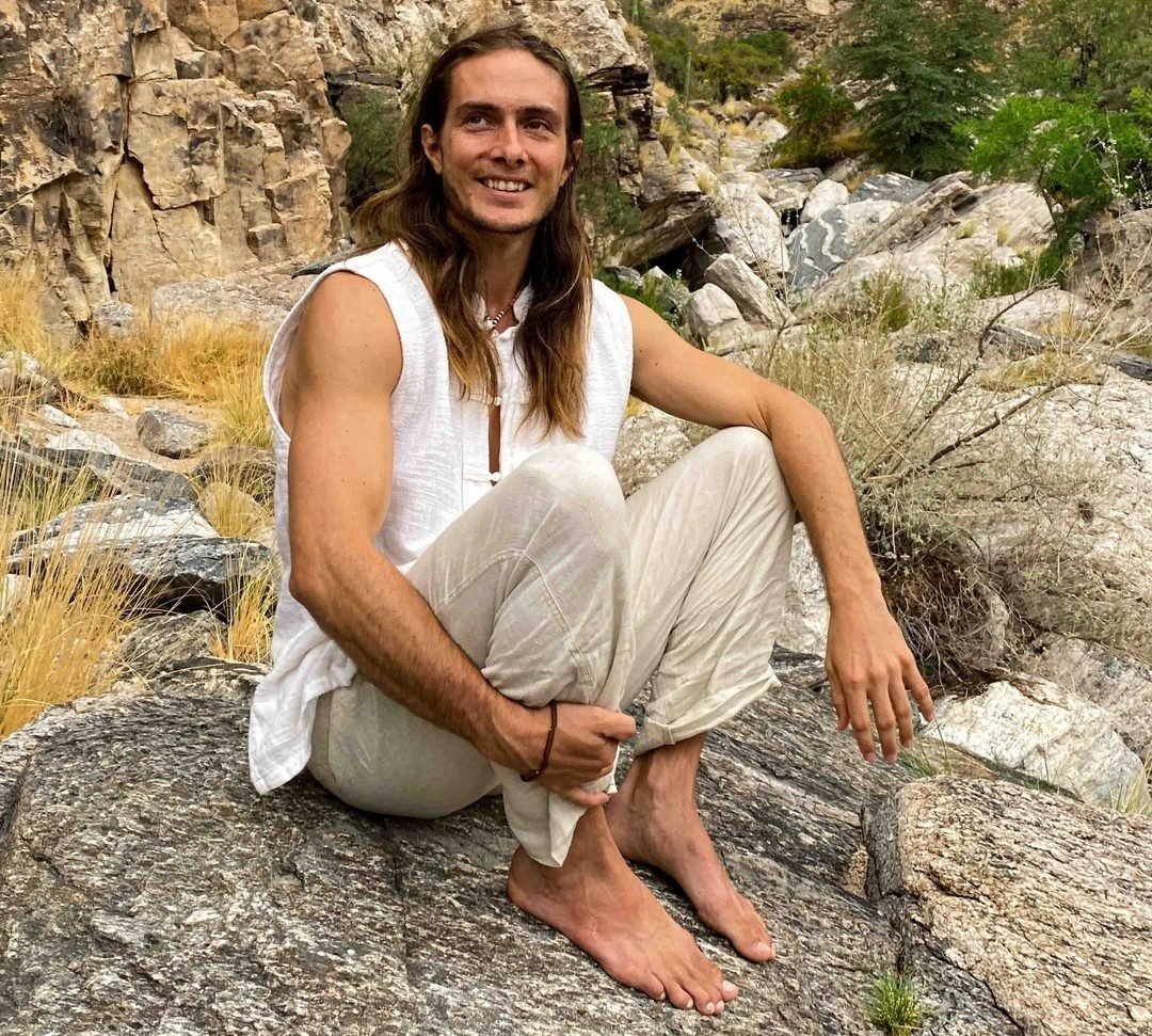 Keith seated barefoot on a rock in a canyon, wearing a white sleeveless shirt.